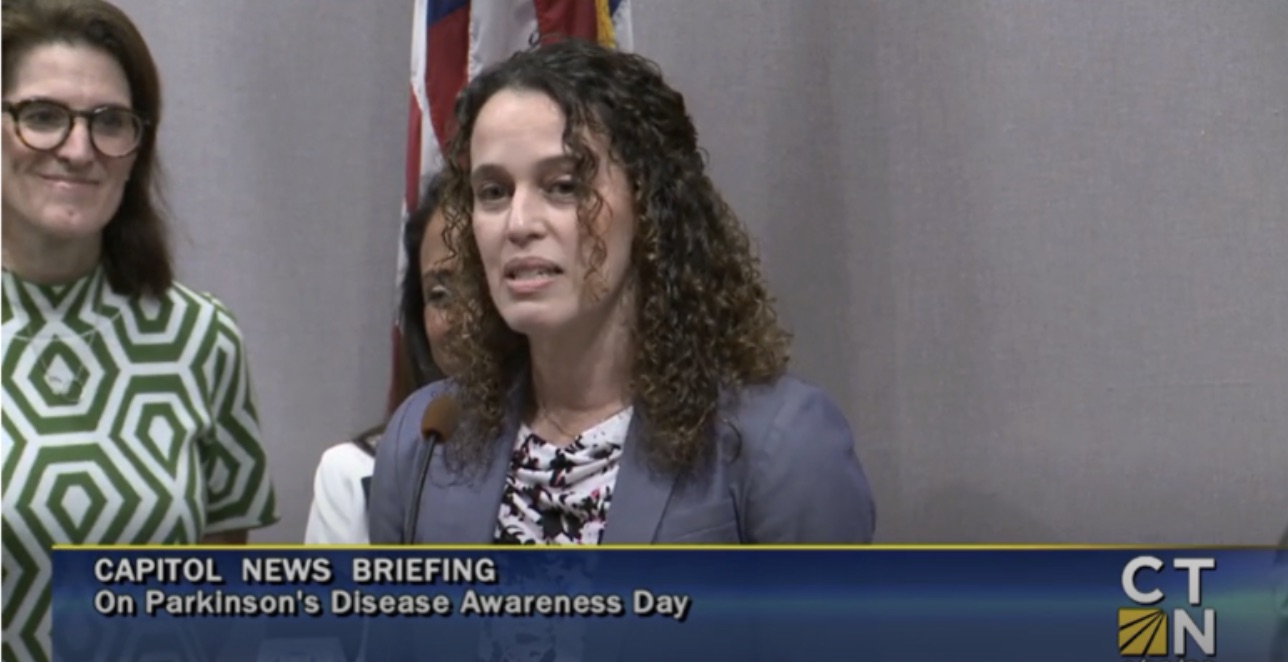 Dr. Colón-Semenza speaking about Parkinson's Disease at a press conference. Caption on screen is "Capitol News Briefing On Parkinson 's Disease Awareness Day".